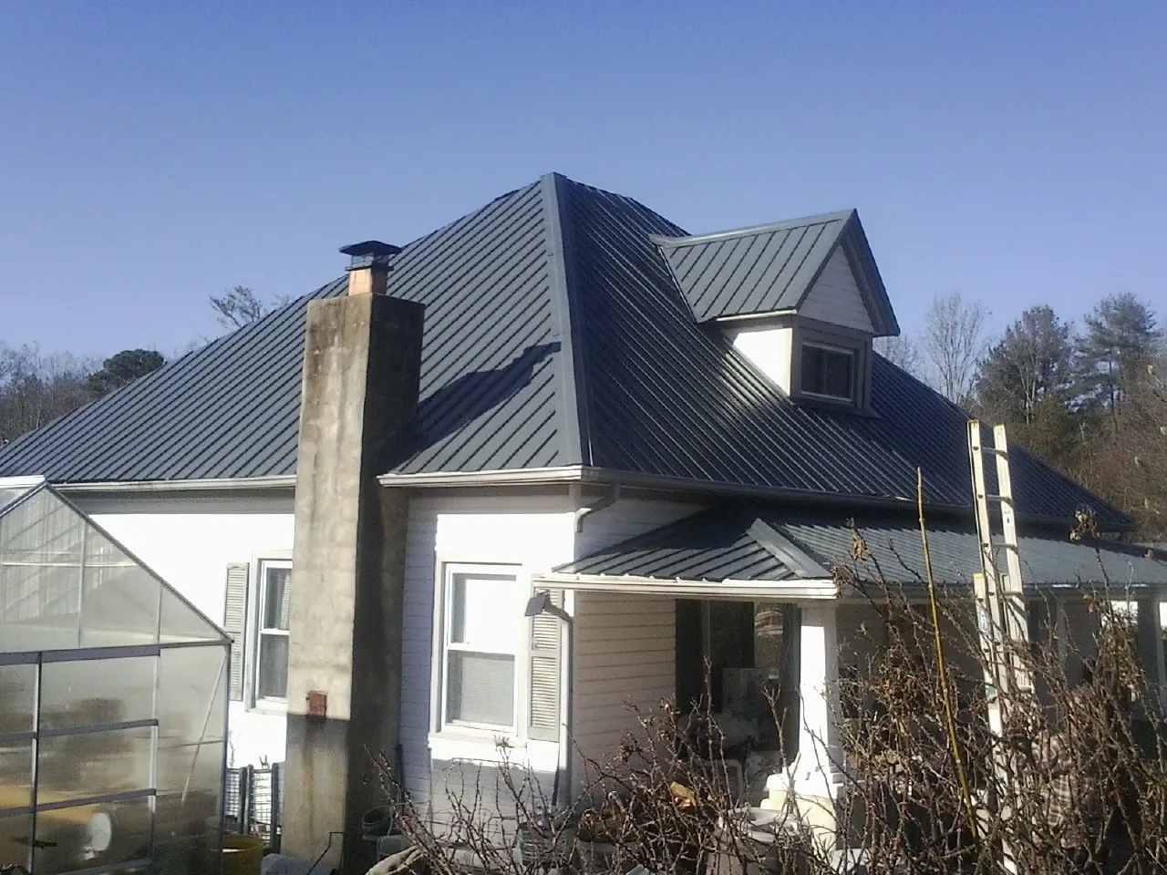 Dark blue standing seam metal roof on a white farmhouse with dormer — Slate & Tile Roof Repair by Roofing Brothers in Duff