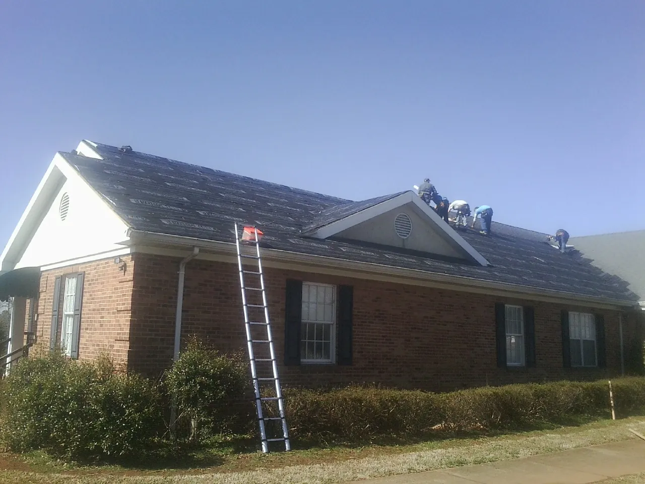 Crew tearing shingles off a brick ranch roof with a ladder set — Emergency Roof Repair work by our crew in Duff