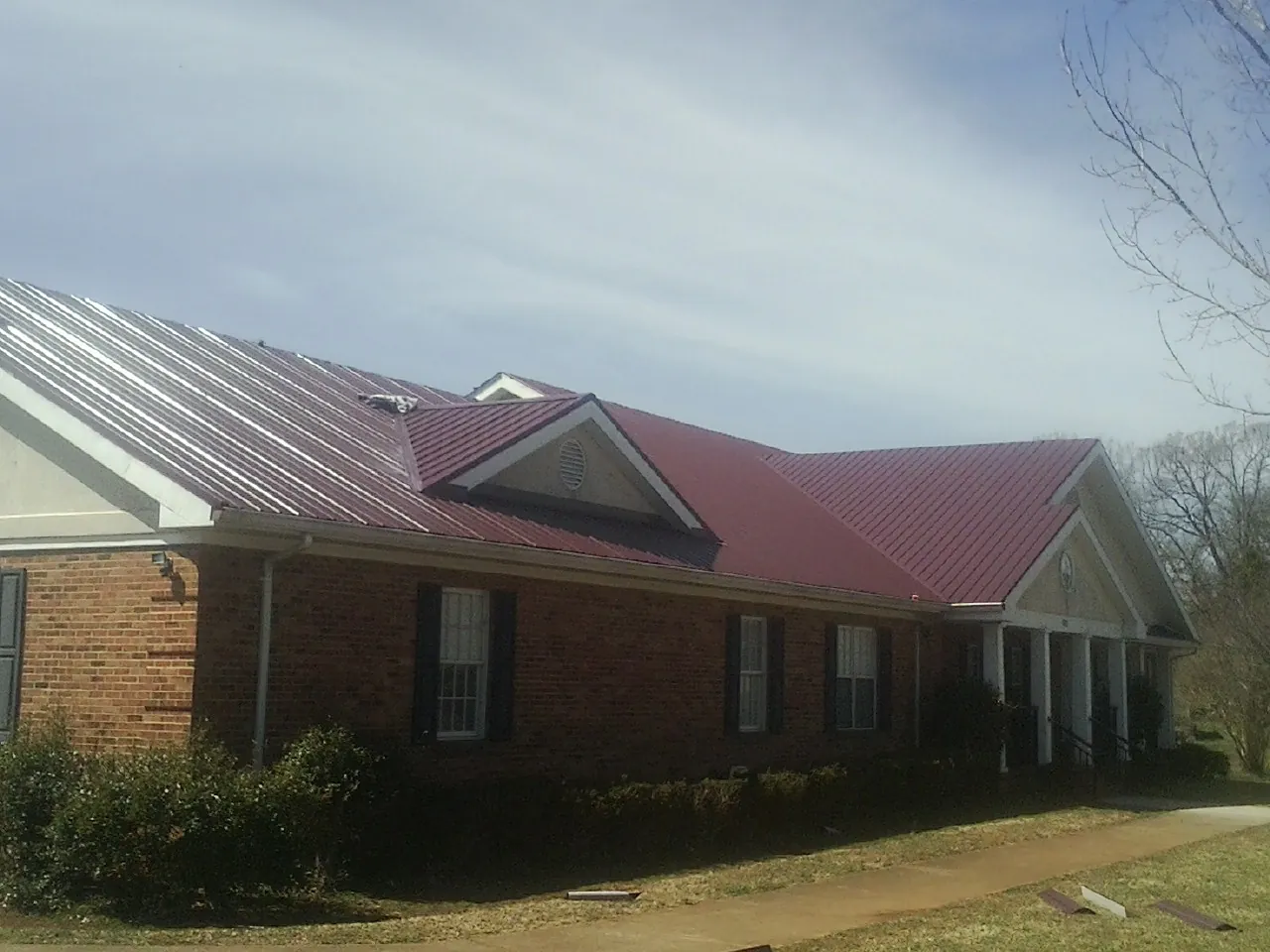 Red metal roof with gabled entries on a long brick building, from a Hail Damage Roof Repair job in Duff