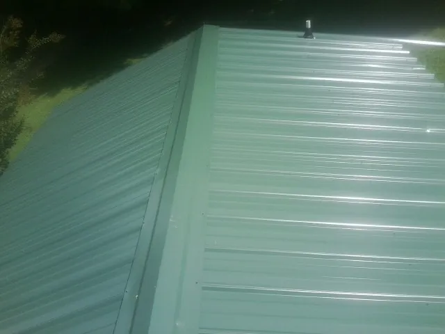 New green metal panels meeting at the ridge of a roof — Flat Roof Repair work by our crew in Duff