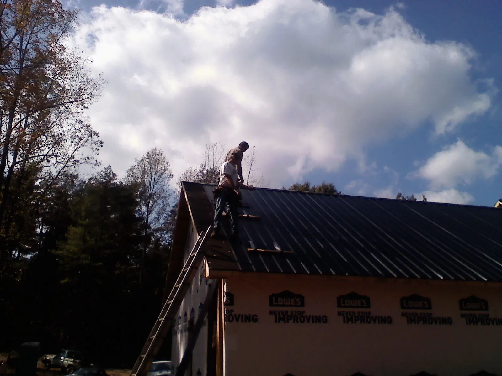 Roofer fastening dark metal panels high against a cloudy sky, from a Roof Inspection job in Duff
