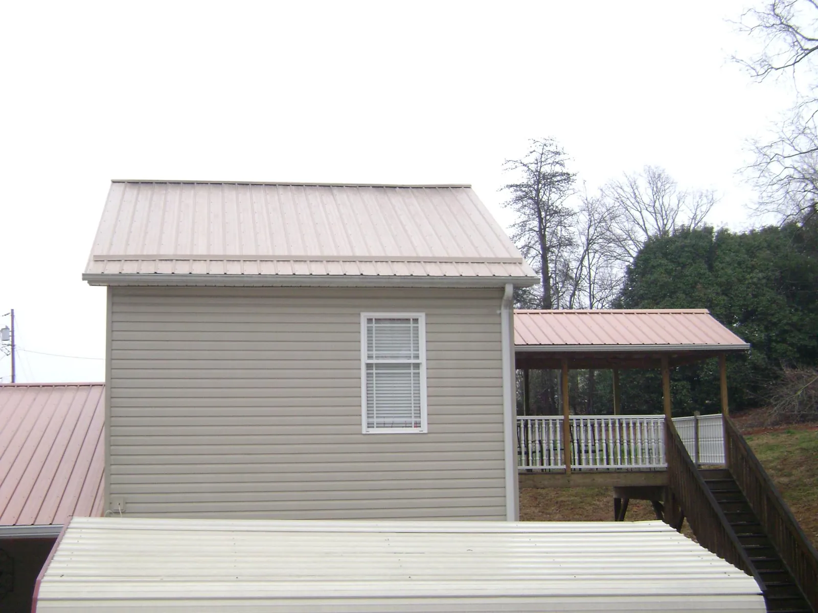 Tan metal roofs on a two story addition and attached porch, from a Roof Replacement job in Duff